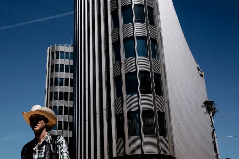 man wearing a hat standing in front of a building street photography of a person, by efi logginou