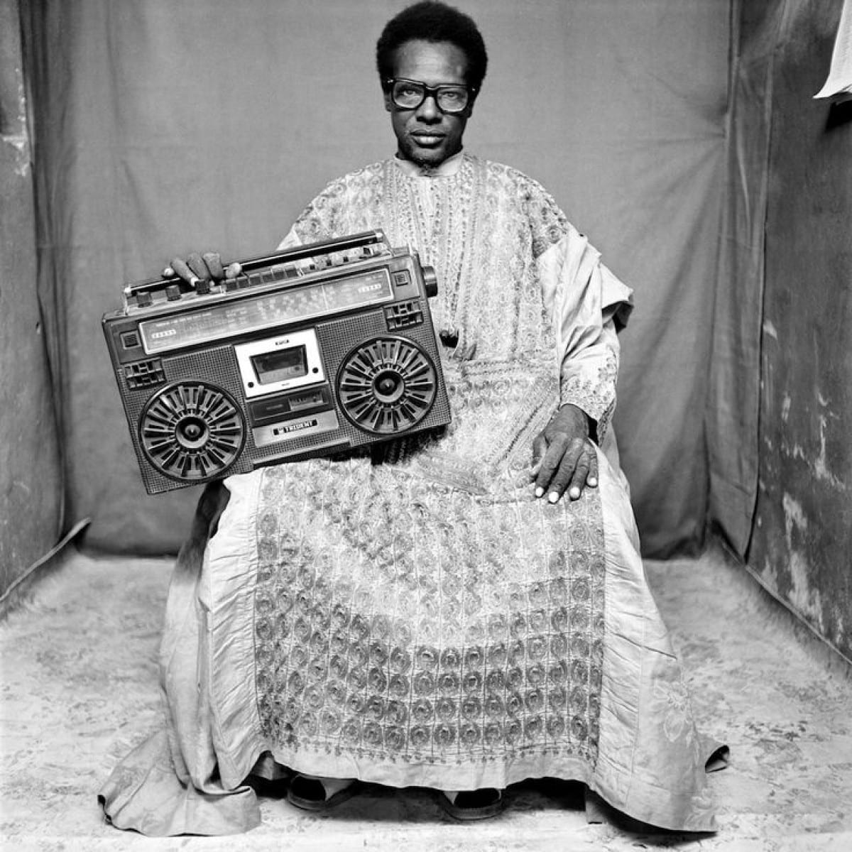 Black & white portrait photography by Seydou Keita. Man holding a boombox in traditional outfit, in Mali