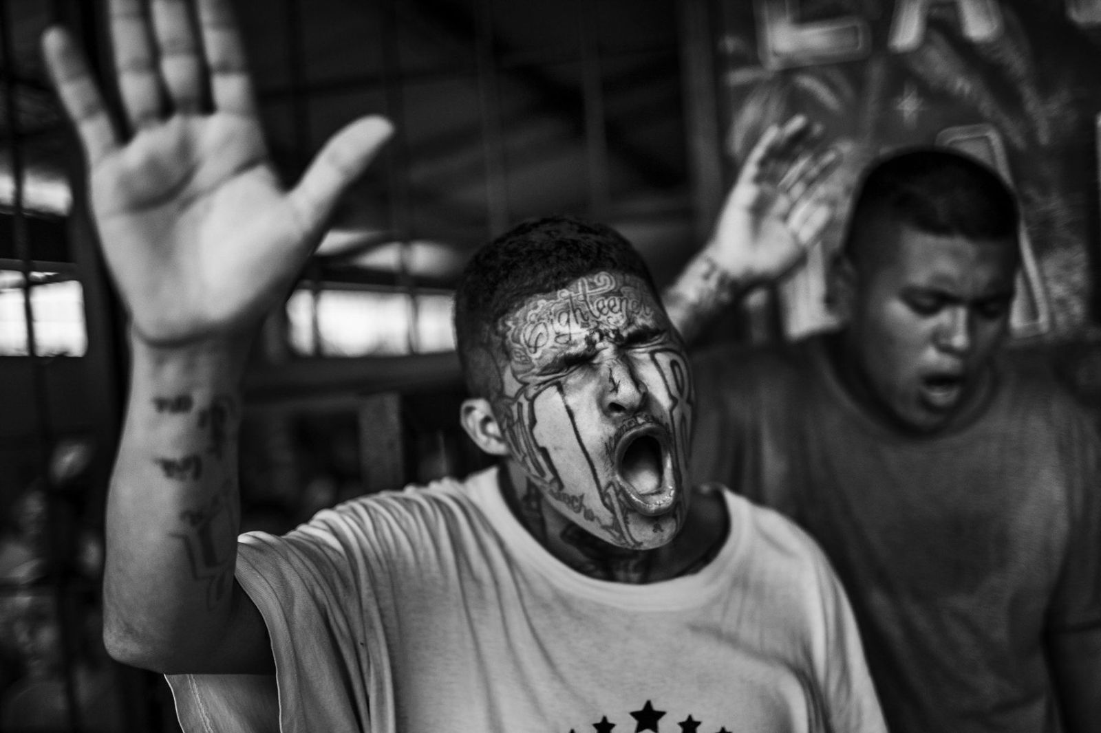 Black and white photo by Javier Arcenillas - 'Maras Gang Member Praying'. San Francisco Gotera jail, El Salvador. From long term project 'Latidoamerica'