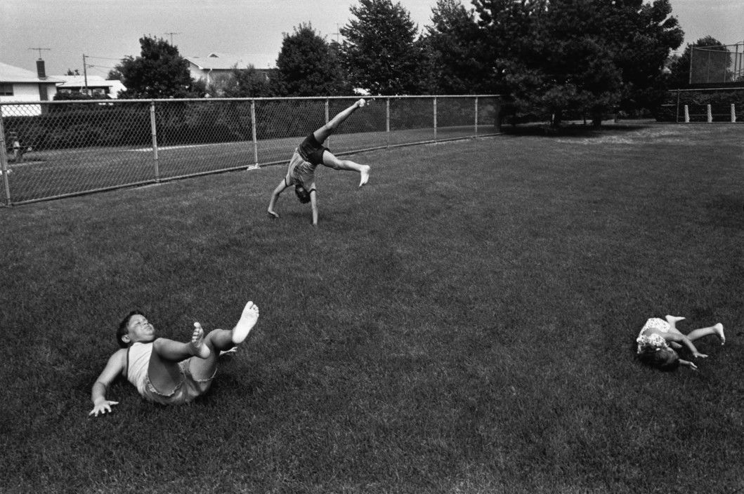 Black and white street photography by Richard Kalvar of kids playing in the grass. Shot in New York, Long Island