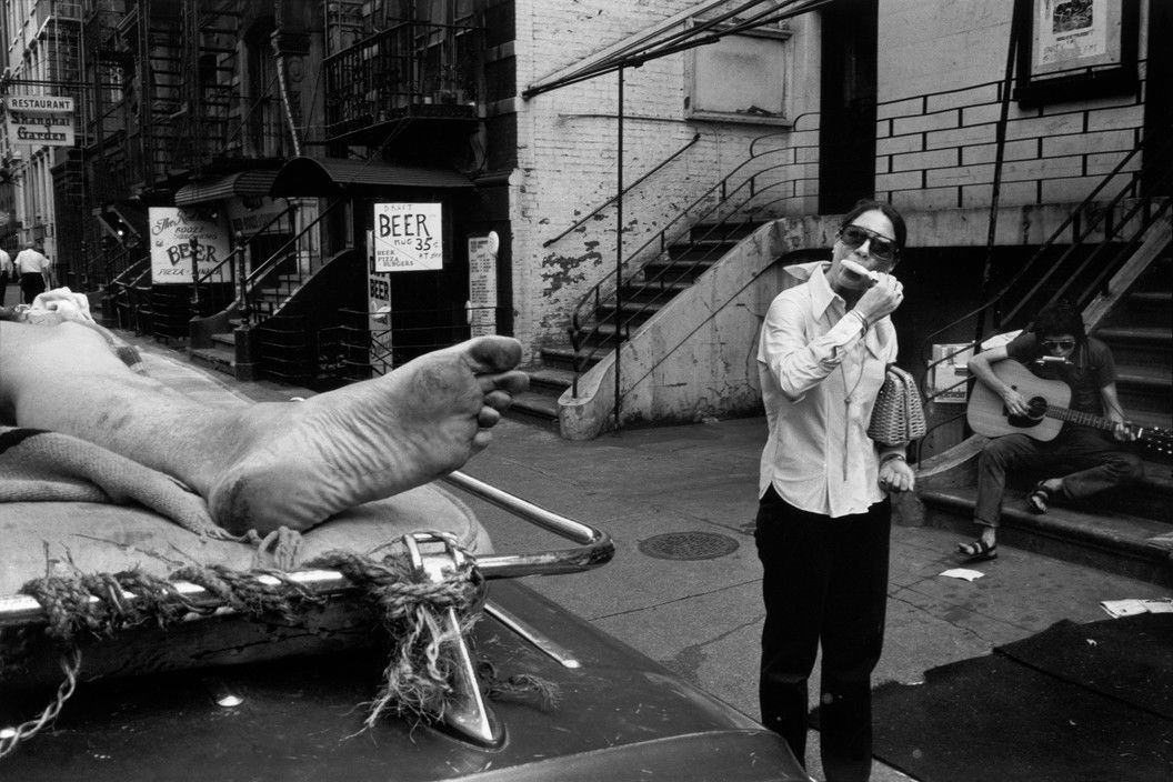 Black and white street photography by Richard Kalvar, a leg, a woman eating an ice cream and a man playing guitar in New York City.