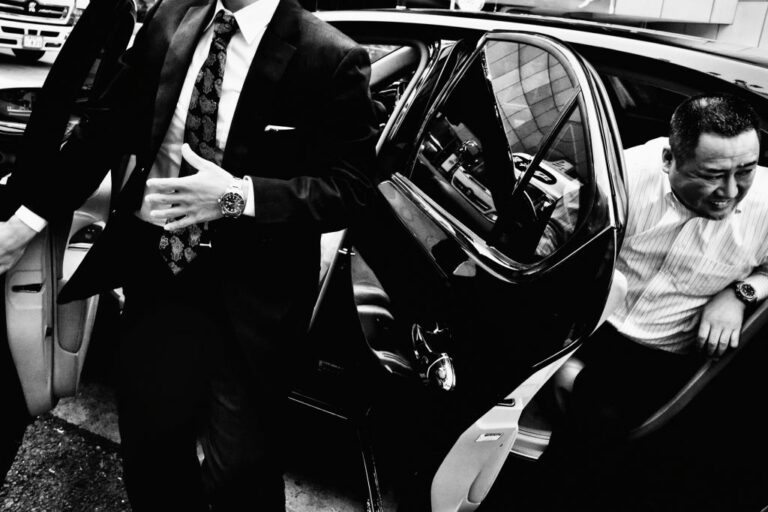 Black and white street photography by Tatsuo Suzuki. two men, car, Tokyo Japan