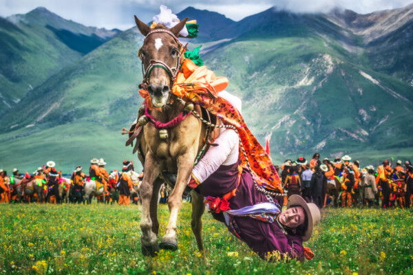 Color photo of an acrobatic horse rider with mountains in the backdrop in Tibet