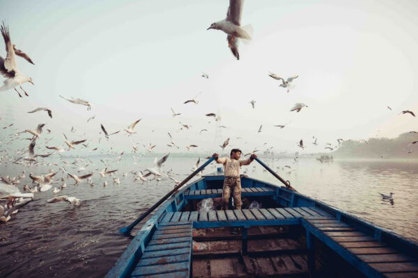 color street an documentary photo of a boy rowing a small wooden boat on Yamuna river in India by Vikas Datta