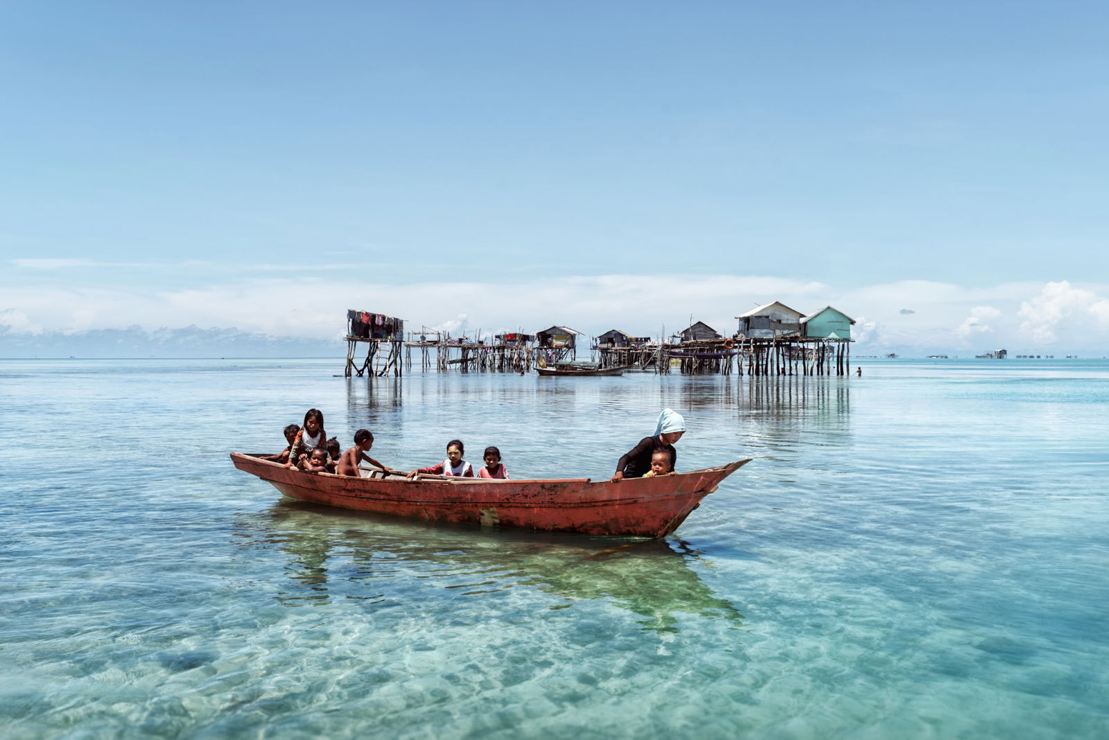 Documentary photography by Jacopo Della Valle. Children on a boat with wooden stilt houses in the background. From his project, "Waterworld".