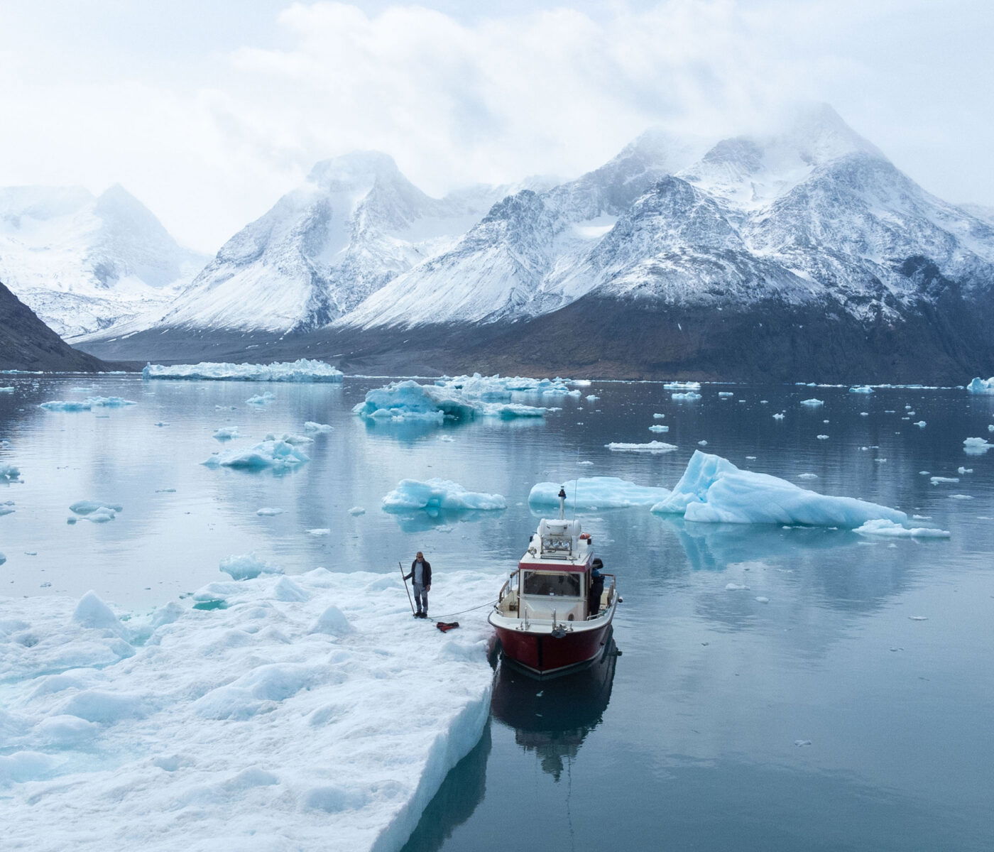 Photo of an Inuit man next to a boat and a Fjord in greenland