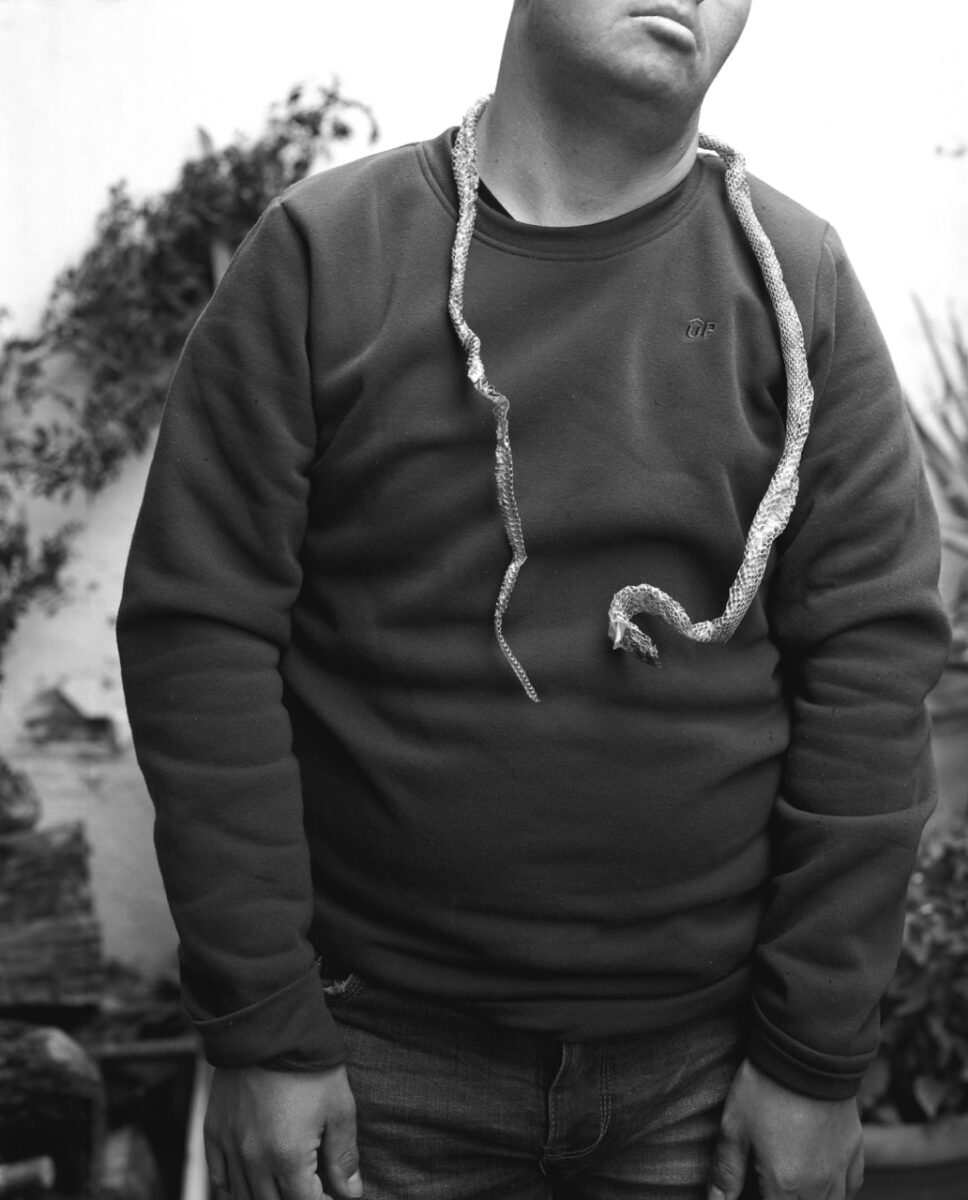 Black & white photo of a man with a snakeskin around his neck by Juan Miguel Ramírez-Suassi