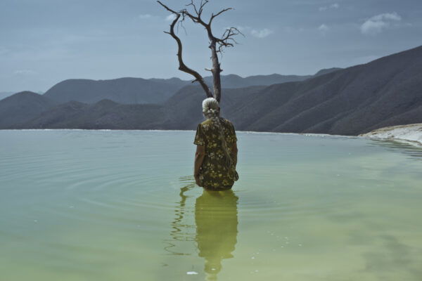 Photo of an elderly woman up to her waist in a lake surrounded by mountains by Cristina de Middel. From the book, Journey to the Center