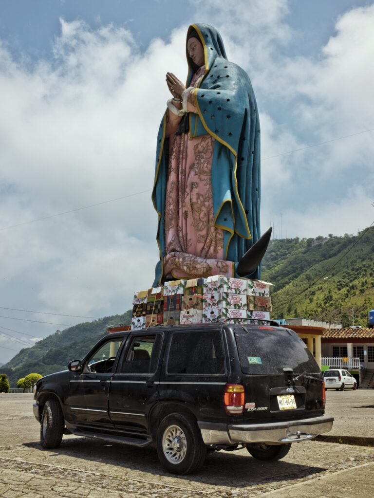 Photo of a car with a giant virgin statue in the background by Cristina de Middel