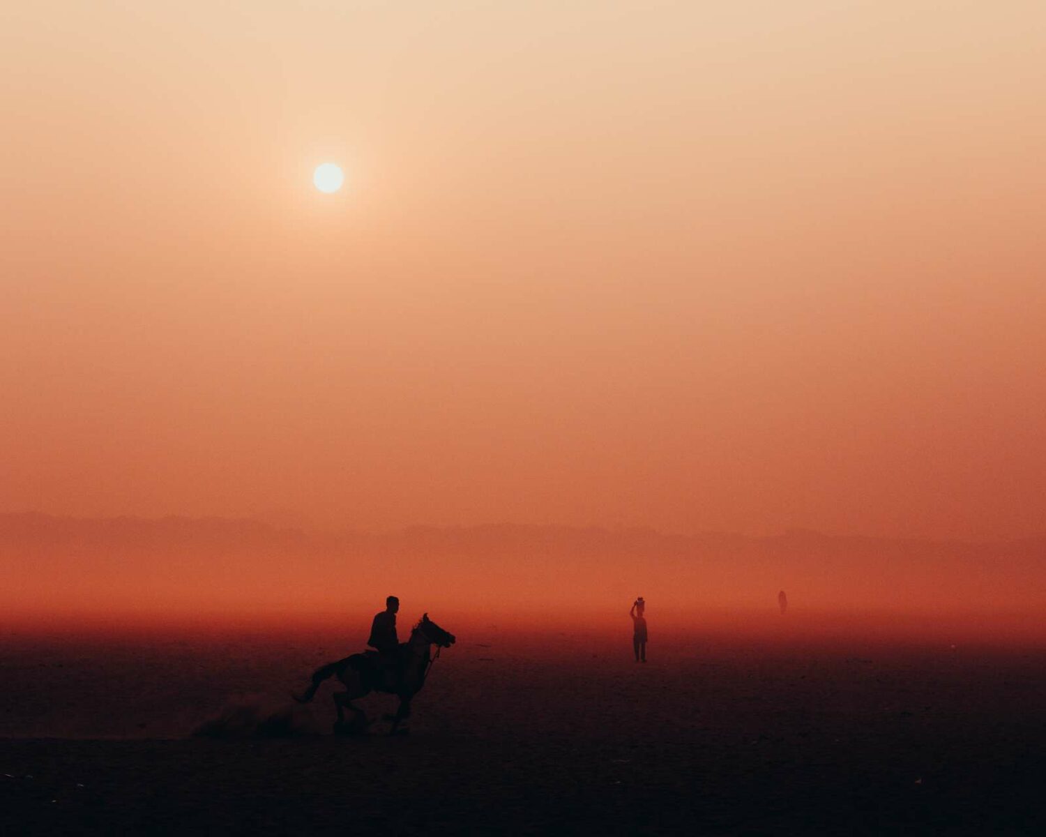 Photo of silhouetted man on a horse and other people in the background at sunset