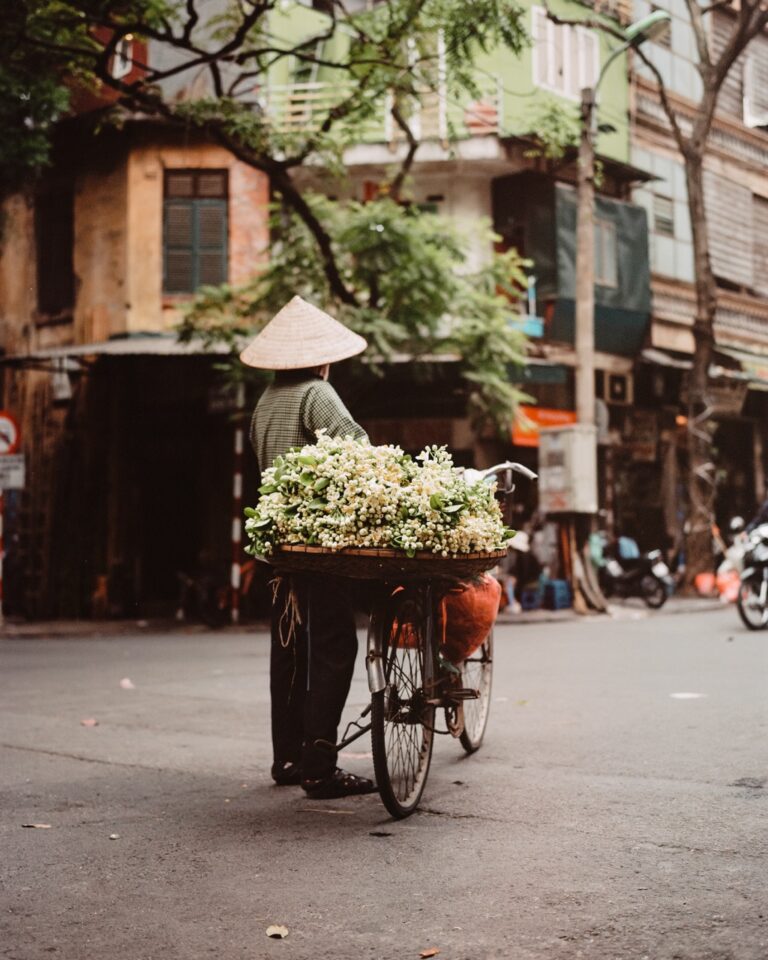 Street photography by Pie Aerts. Woman flower seller in Vietnam stops in the road with flowers on her bicycle