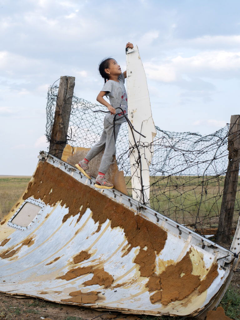 Documentary photography by Andrew McConnell. A girl plays on space junk near her home in Kenjebai-Samai, Kazakhstan 2022