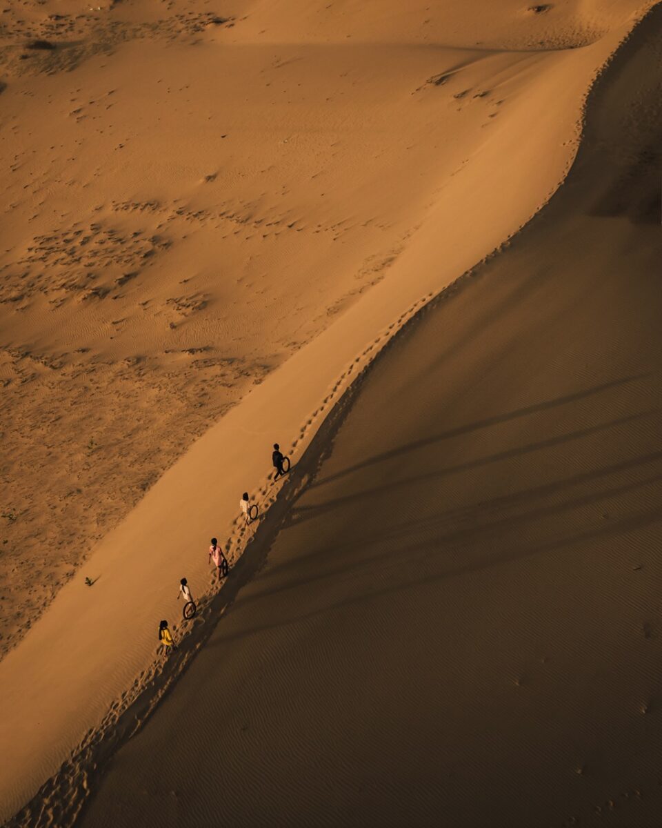 Color travel photography by Mahendra Bakle. Aerial photo of people riding camels through a desert