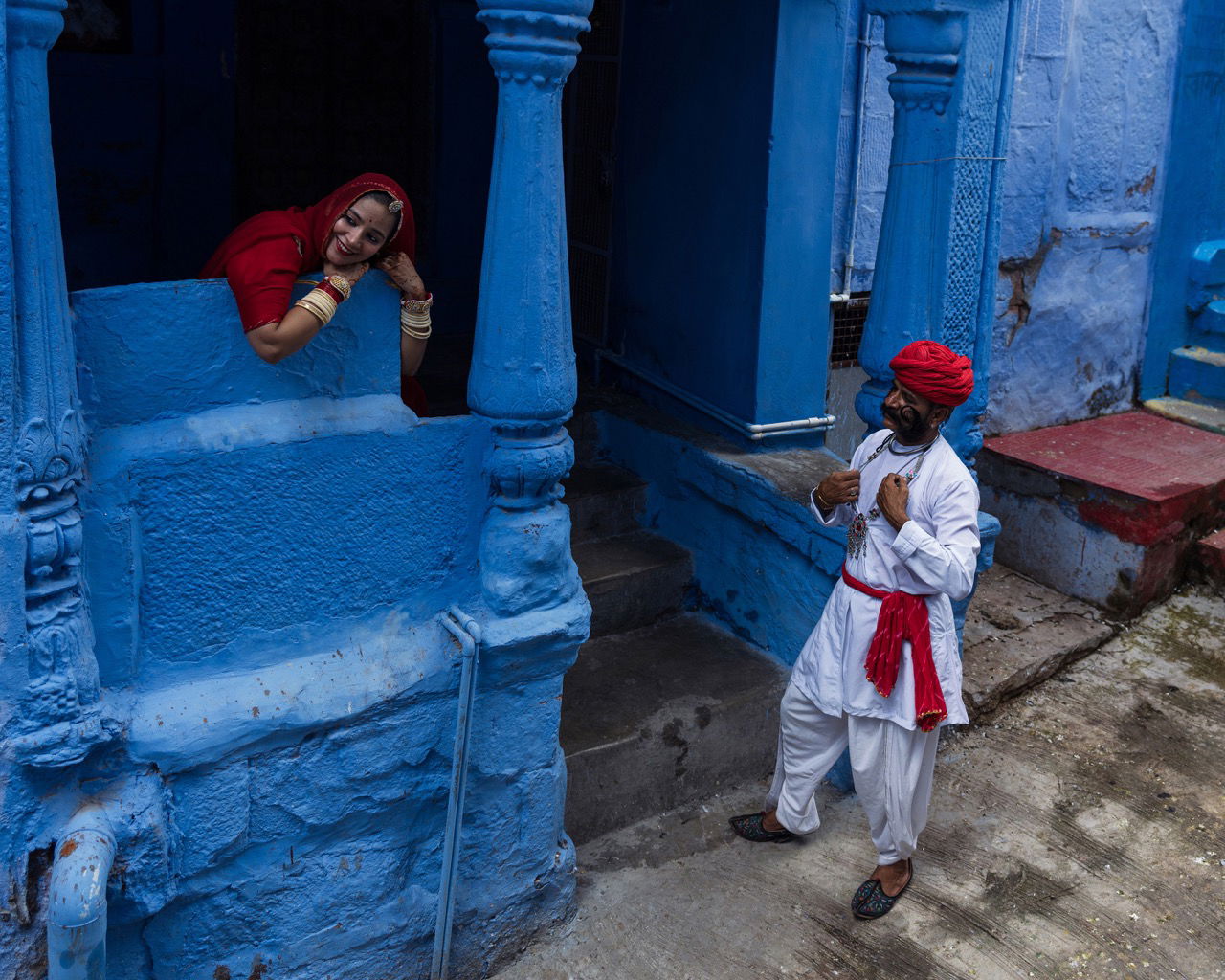 Color travel photography by Mahendra Bakle. Couple in red clothes talking among blue buildings in India