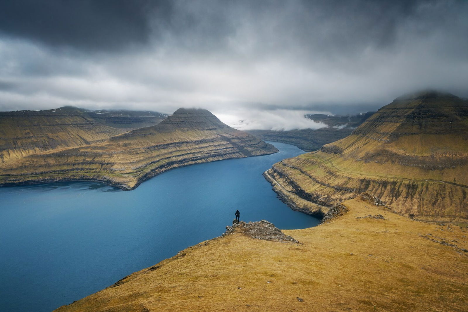 Landscape photography by ​​Jennifer Esseiva. A lake and mountains with the small figure of a man looking over it