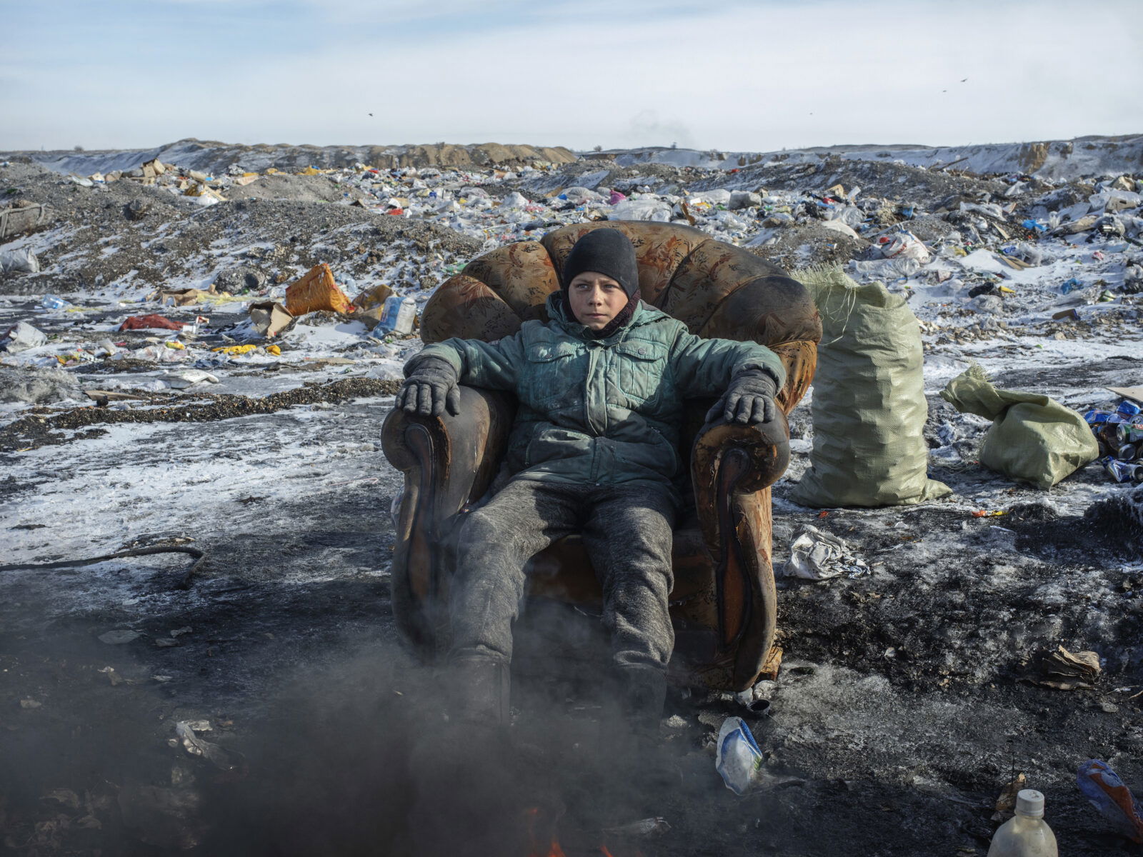 Documentary photography by Andrew McConnell. Portrait of a boy sat in an armchair in front of a field filled with metal. Kazakhstan 2018