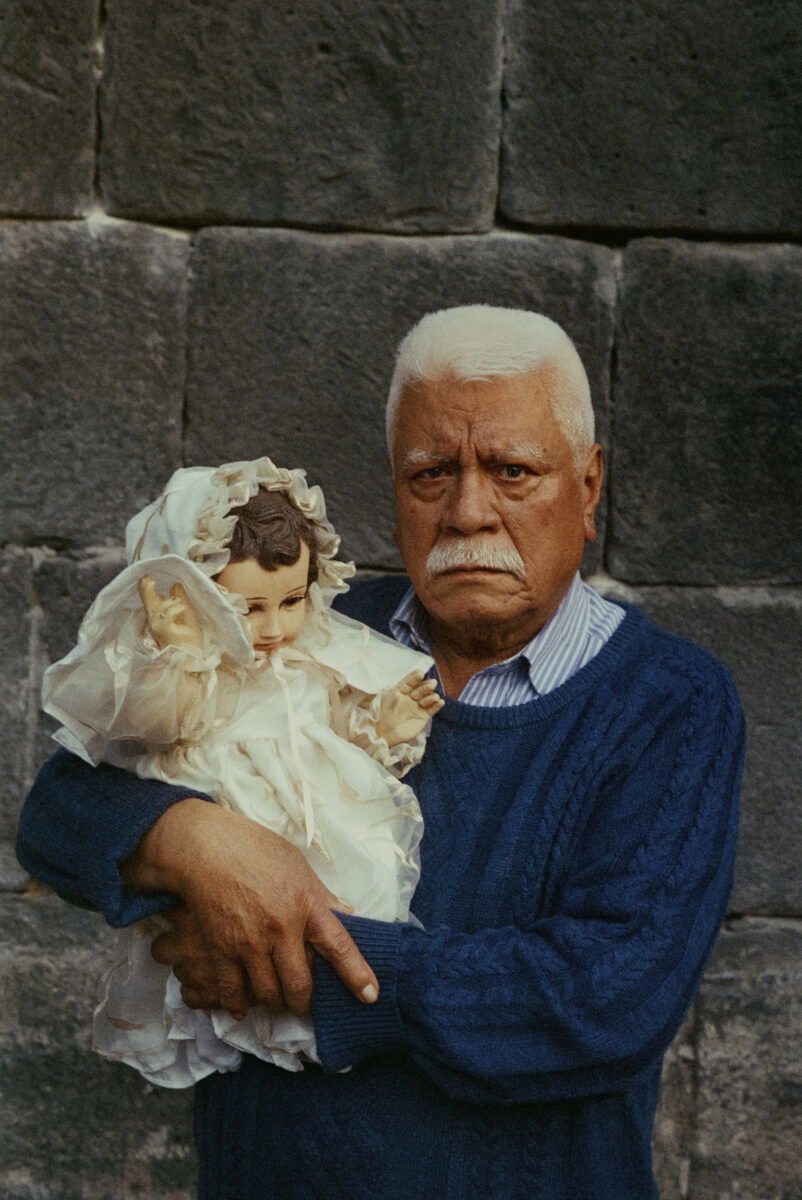 Portrait of an elderly man holding a doll by Marisol Mendez