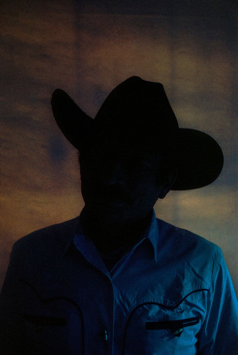 Color photography of a silhouette of a man in a cowboy style hat by Marisol Mendez