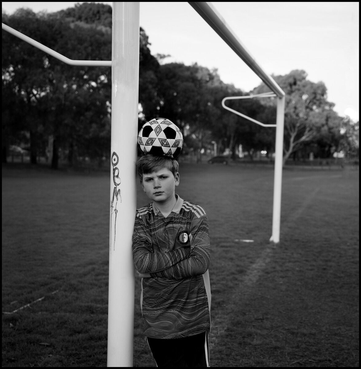 Black and white portrait of a young boy playing football in Melbourne, Australia by Guy Little